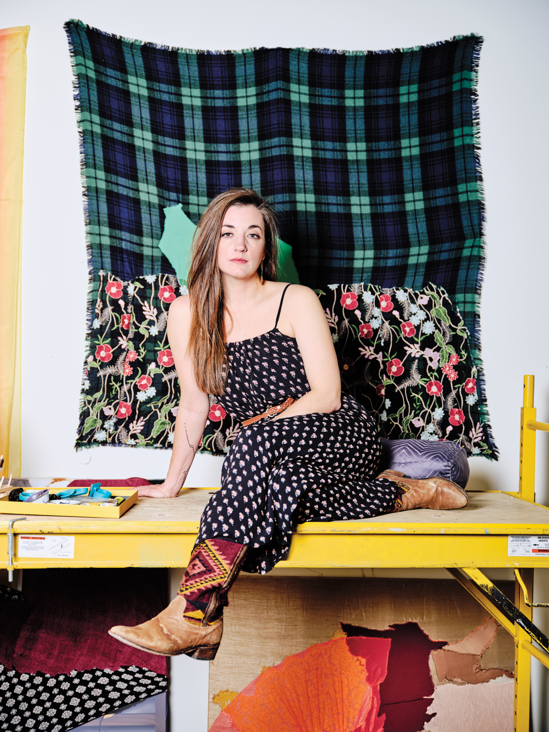 portrait of artist Sarah Darlene Palmeri on a yellow bench with fabric hung behind her