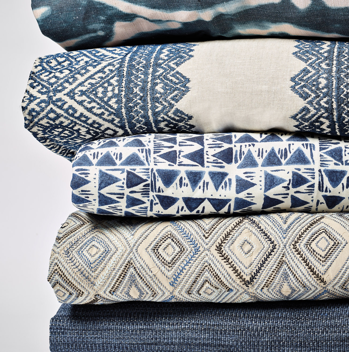 Pile of folded textiles with varying geometric patterns in blue and white shades from Lee Jofa's Breckenridge collection for Kravet.