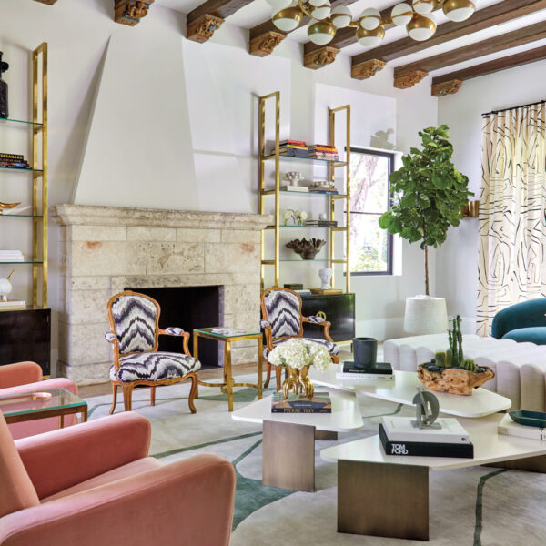 living area with pink armchairs, antique fireplace, teal sofa, white tables and gold étagères