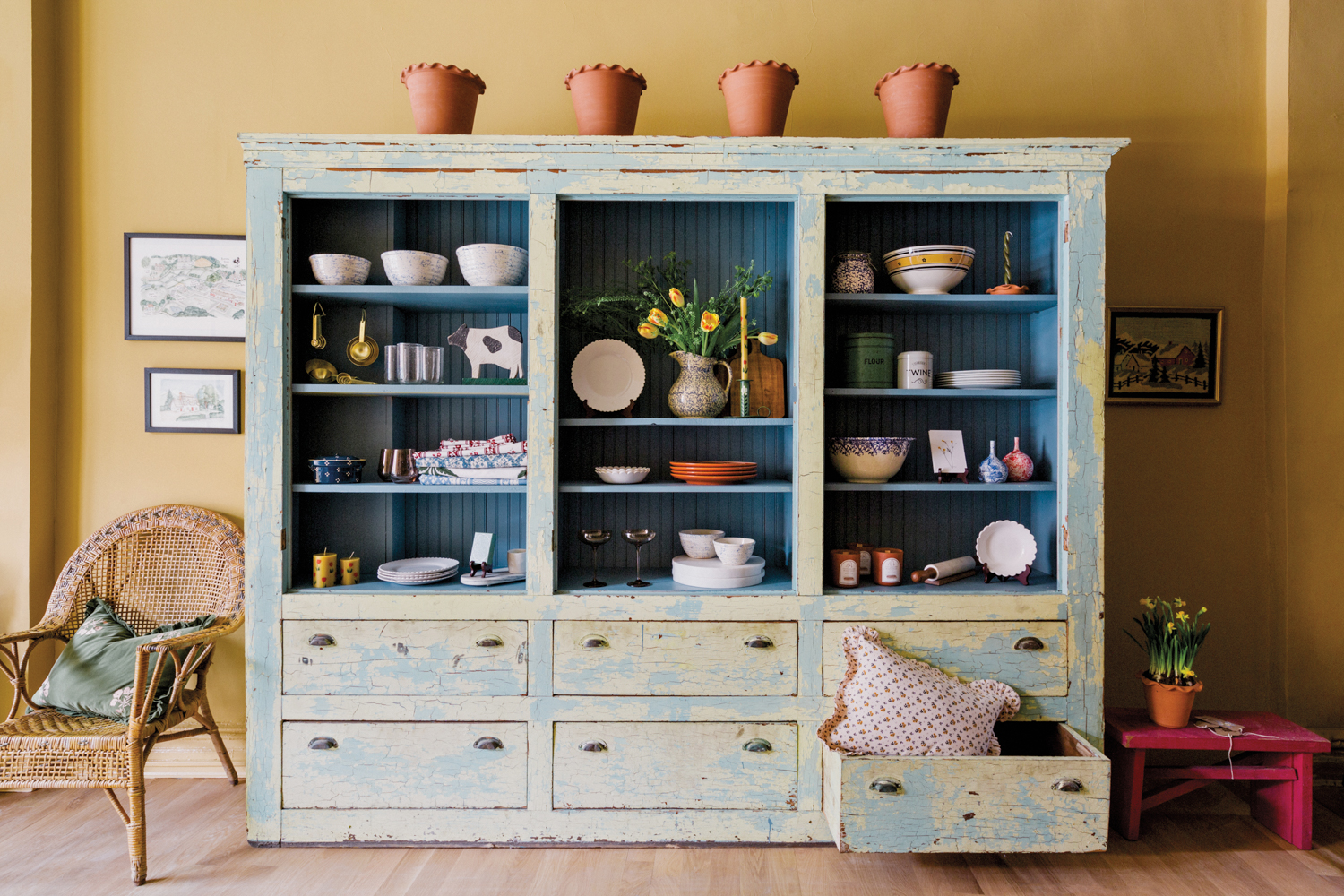 Light blue weathered-wood armoire with homeware display and rattan chair against yellow wall at The Six Bells store