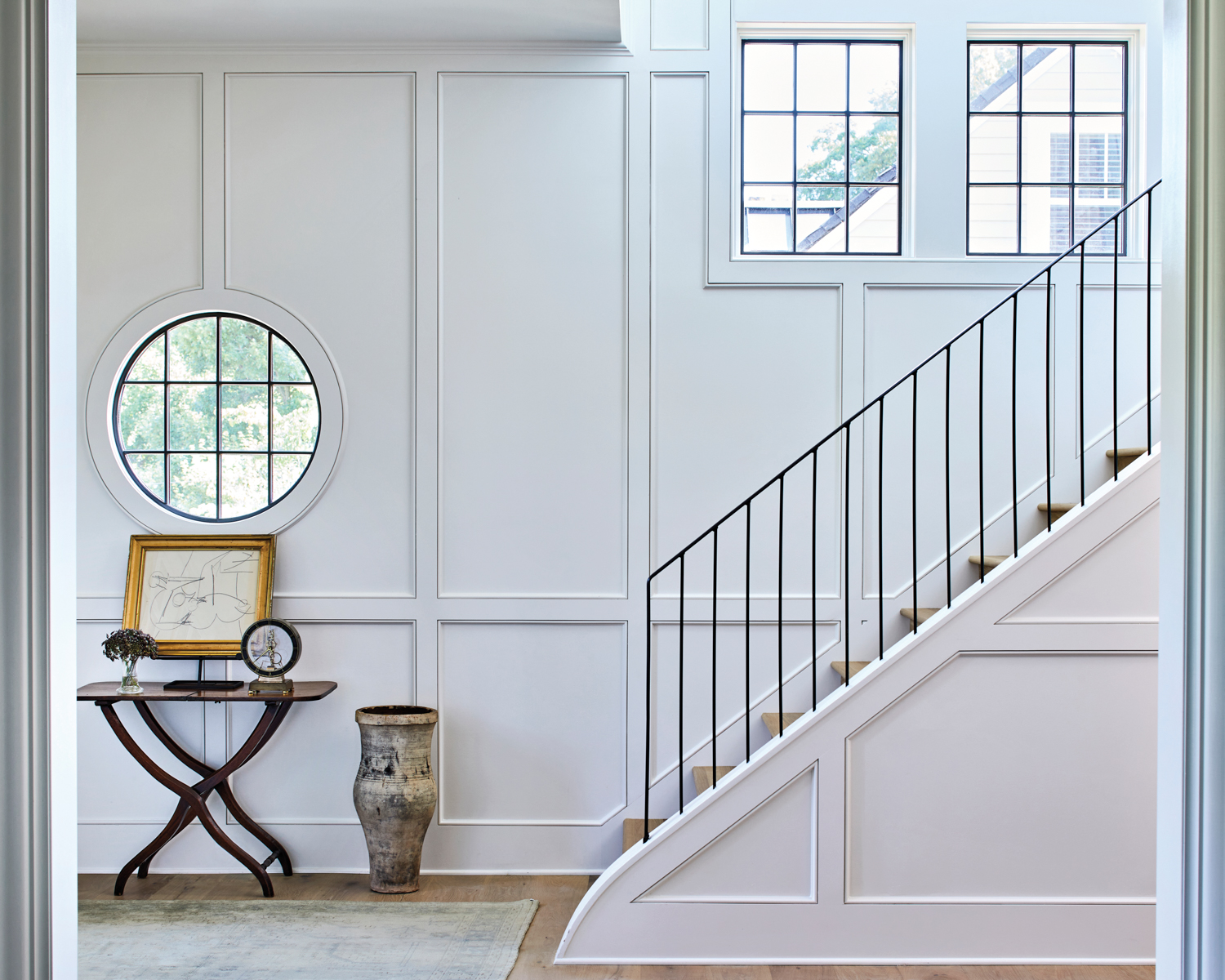 Stair hall with paneled walls, a round window and graceful metal stair railing