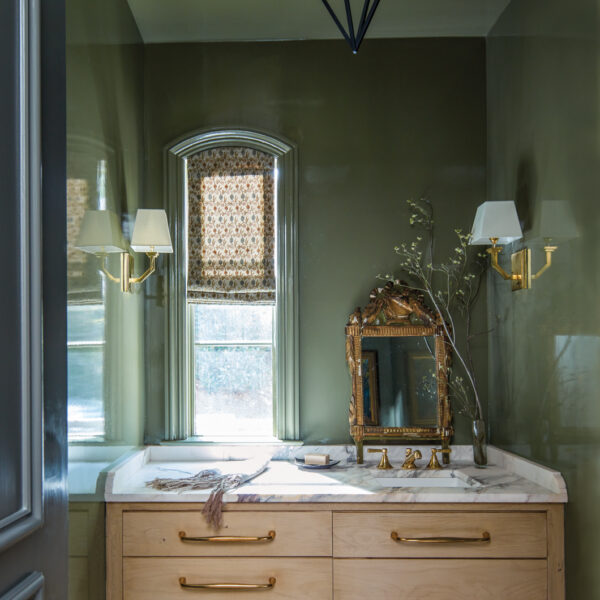 French Country Style Inspires The Revamp Of A Tailored Alabama Abode Small bathroom featuring glossy green walls, white oak cabinetry and an ornate gilt mirror beside a narrow window