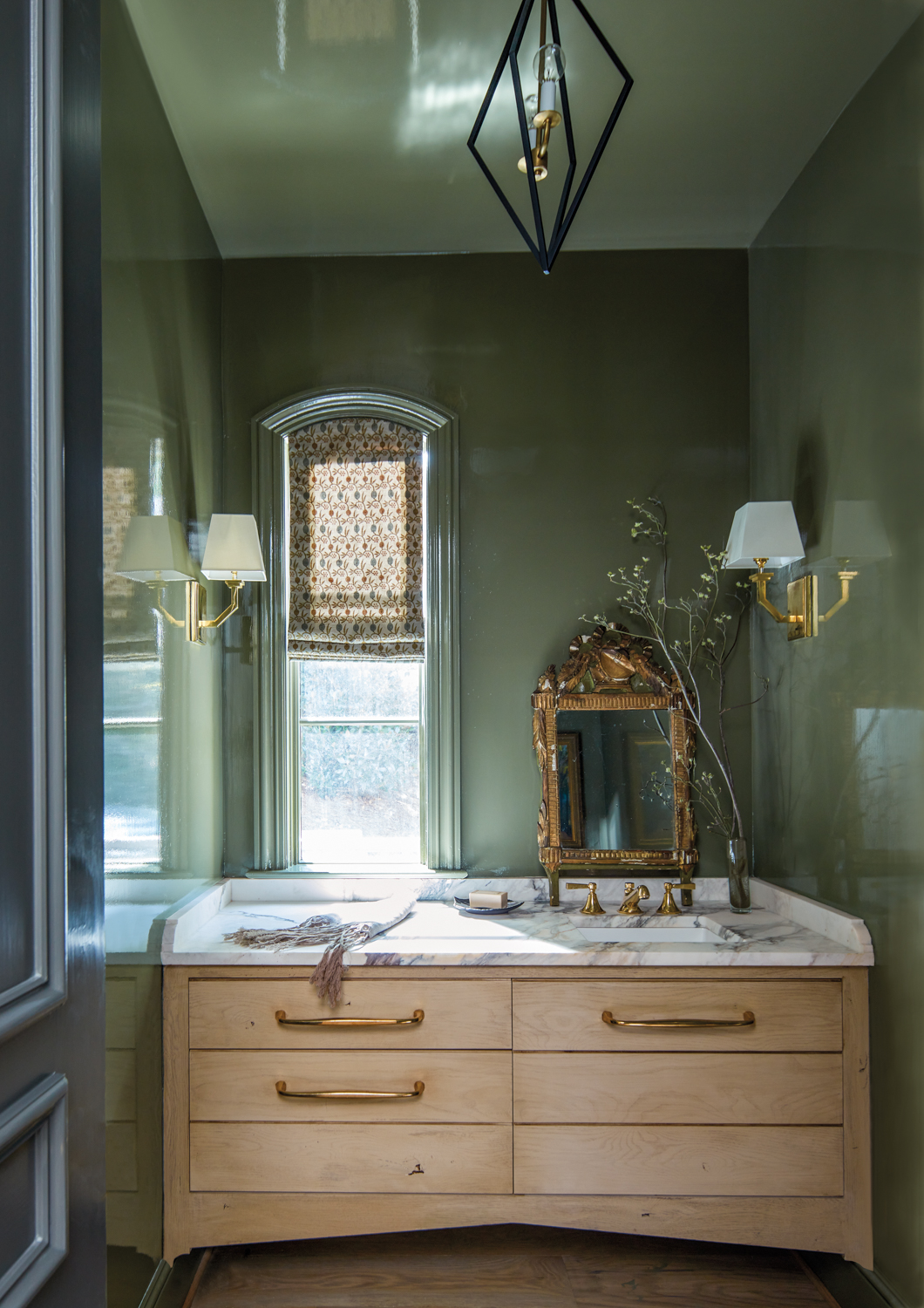 small glossy green bathroom with white oak cabinetry and ornate gilt mirror