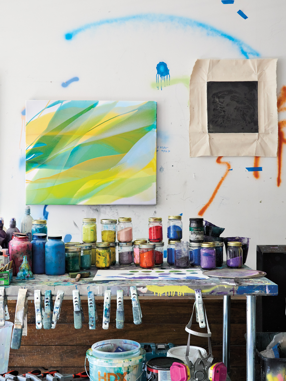Work table with jars of colorful paints; abstract artwork mounted to wall