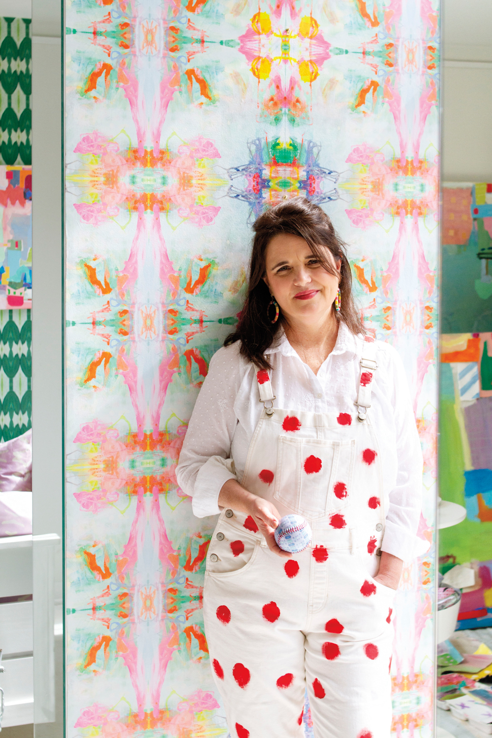 Headshot of artist Cathy Lancaster wearing white apron with red polka dots in front of pink and green artwork.