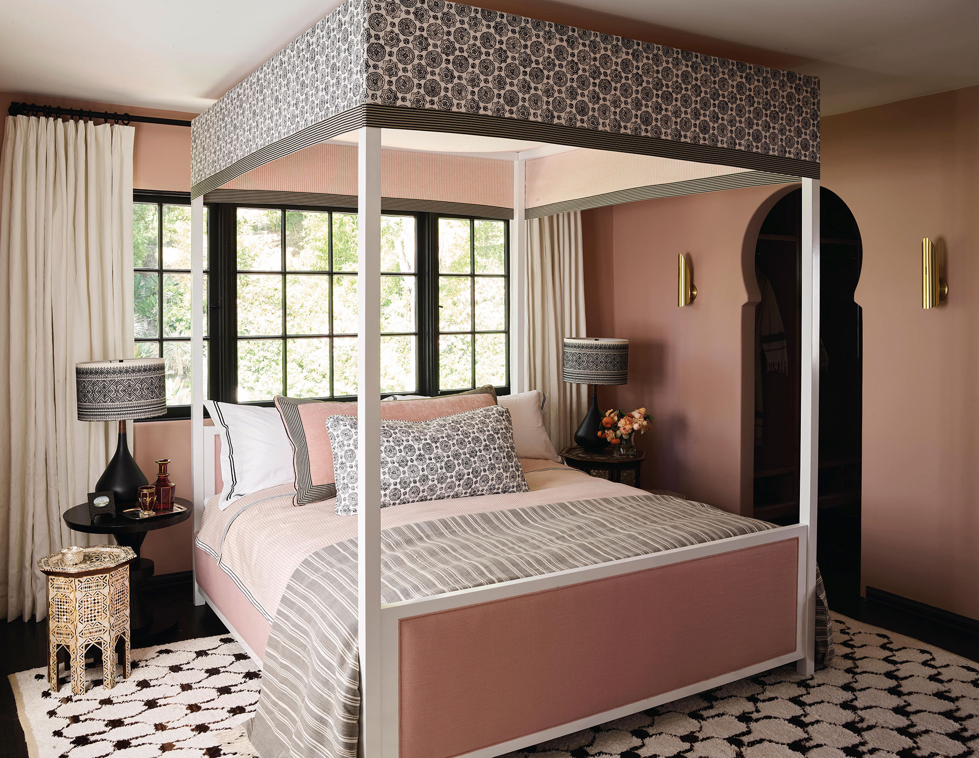 A pink bedroom with a gray-and-white canopy bed and a black-and-white rug.