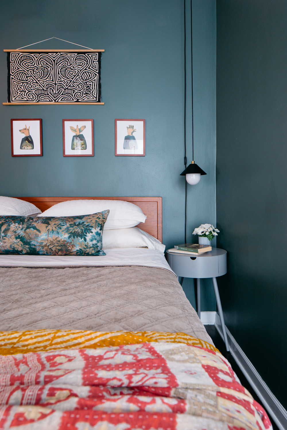 A green bedroom with eclectic art and bed linens in a variety of colors.