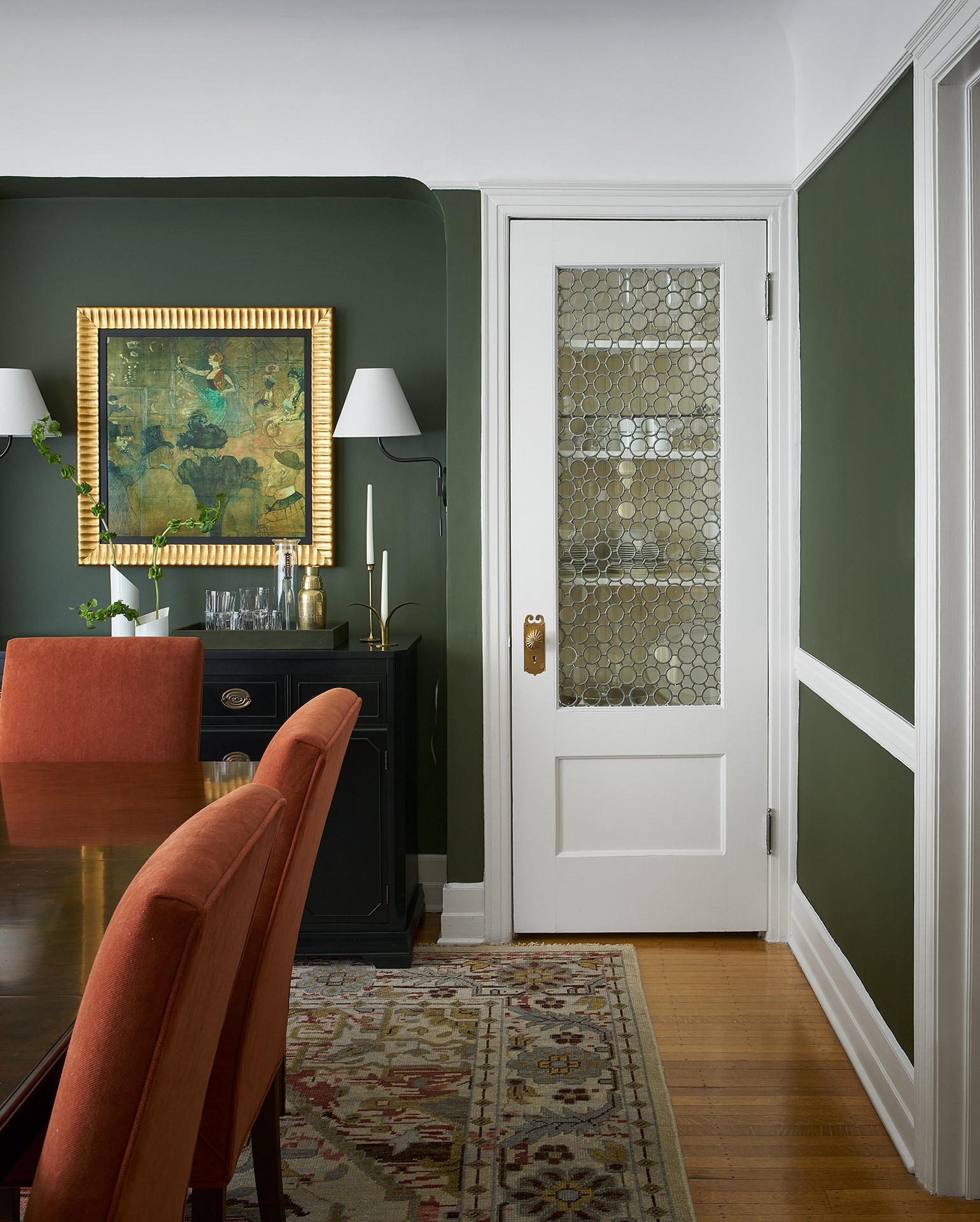 A dining room with green walls and orange chairs.