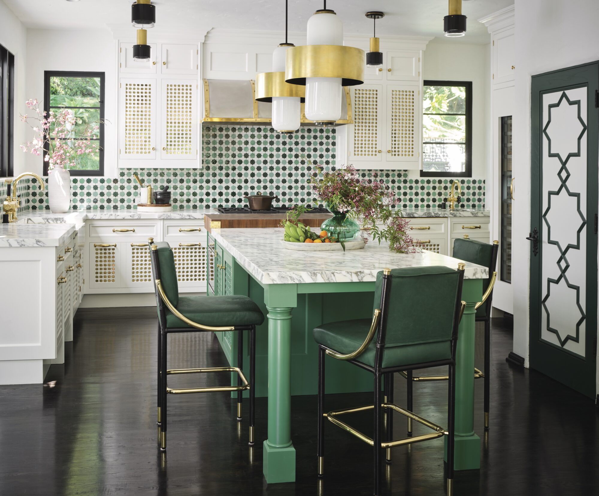 A ktichen with a green, marble-topped island, white cabinetry and a green-and-white backsplash.