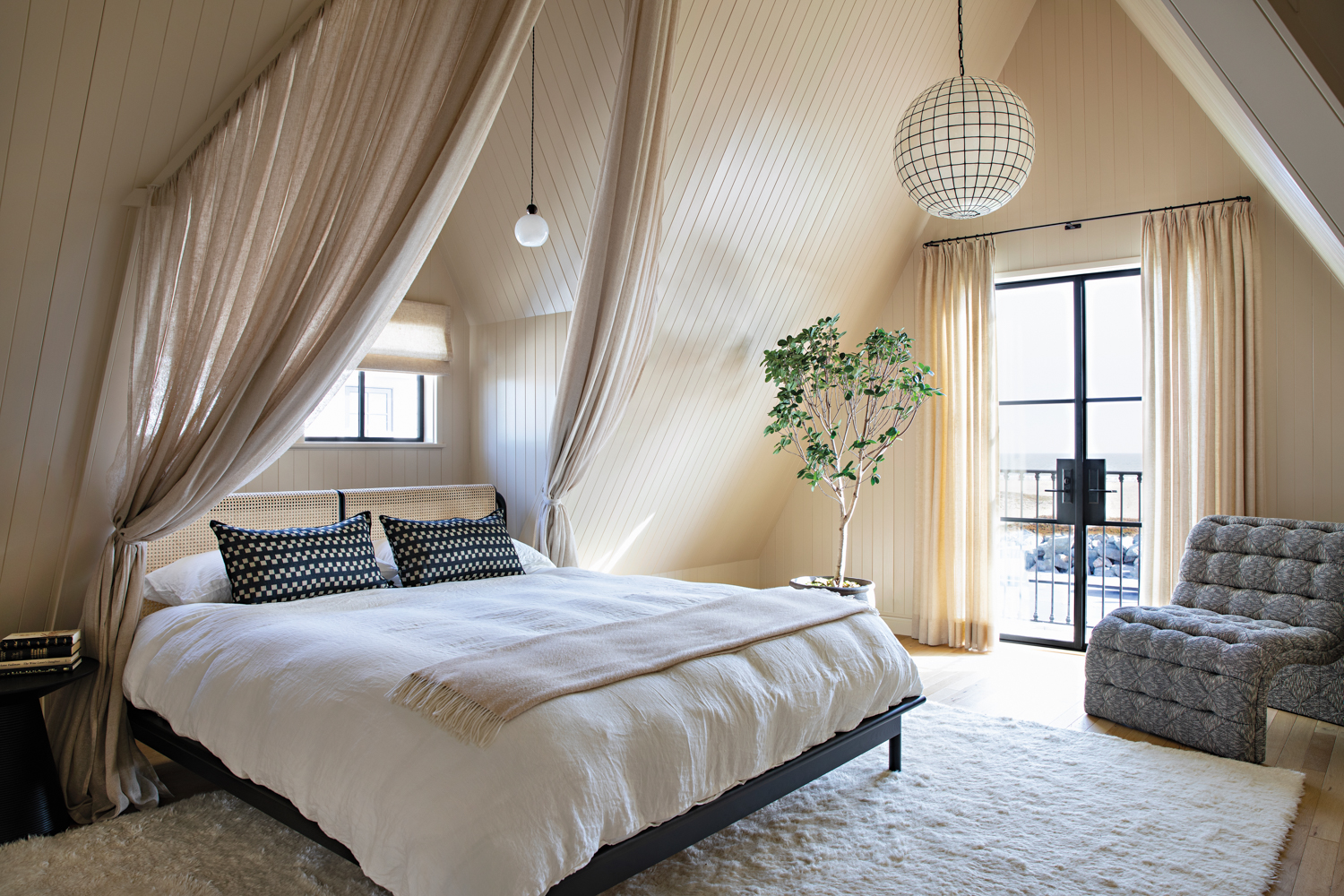 Bedroom with gabled ceilings, drapes around a white bed, sheer window treatments and a wool rug