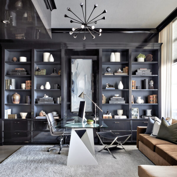 How An Ornate Chicago Penthouse Transformed Into A Chic Bachelor Pad home office with gray shelving, brown couch and a sculptural chandelier above the glass desk