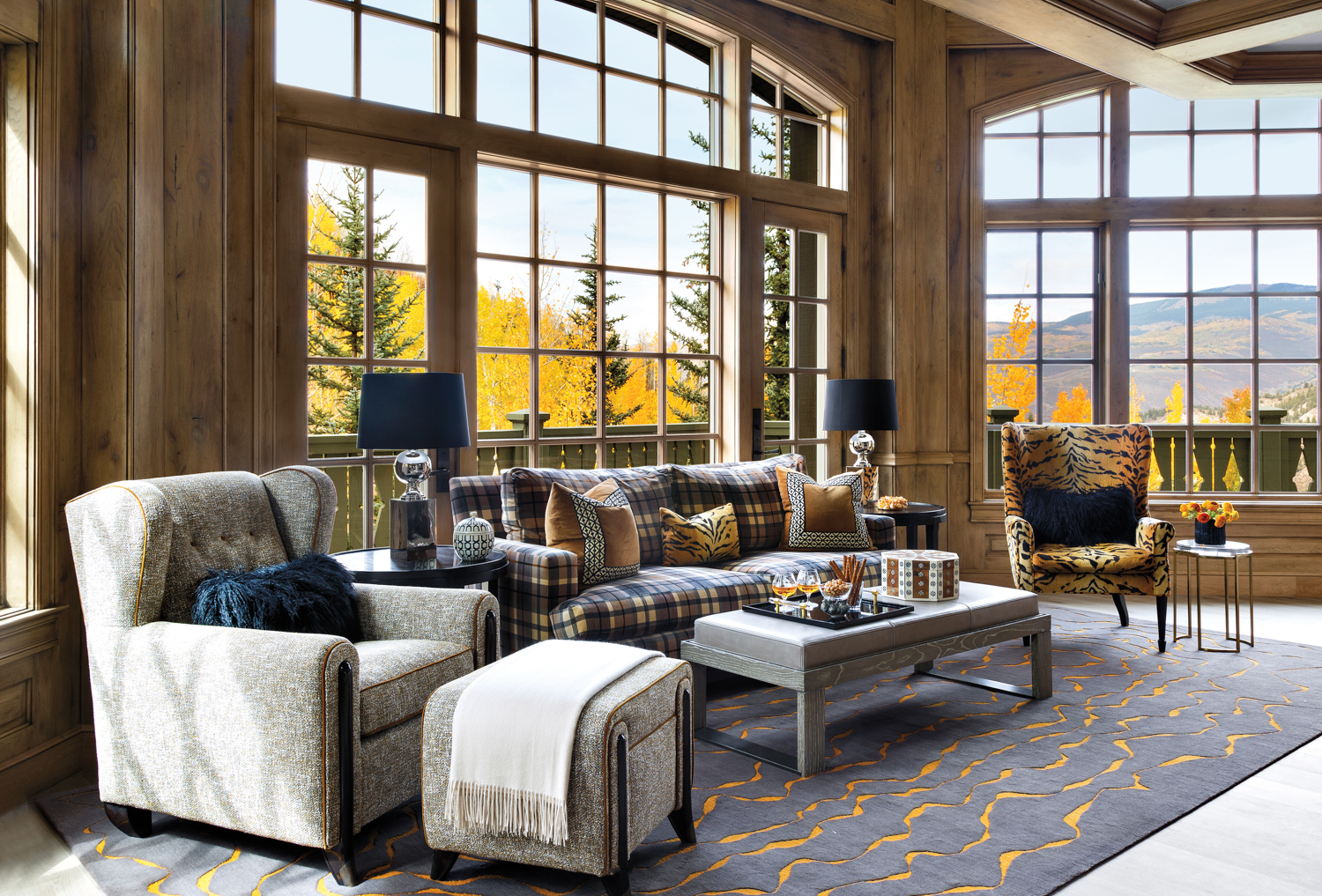 Living room with butternut-wood walls, panoramic views of fall foliage and armchairs and sofa in varied patterns