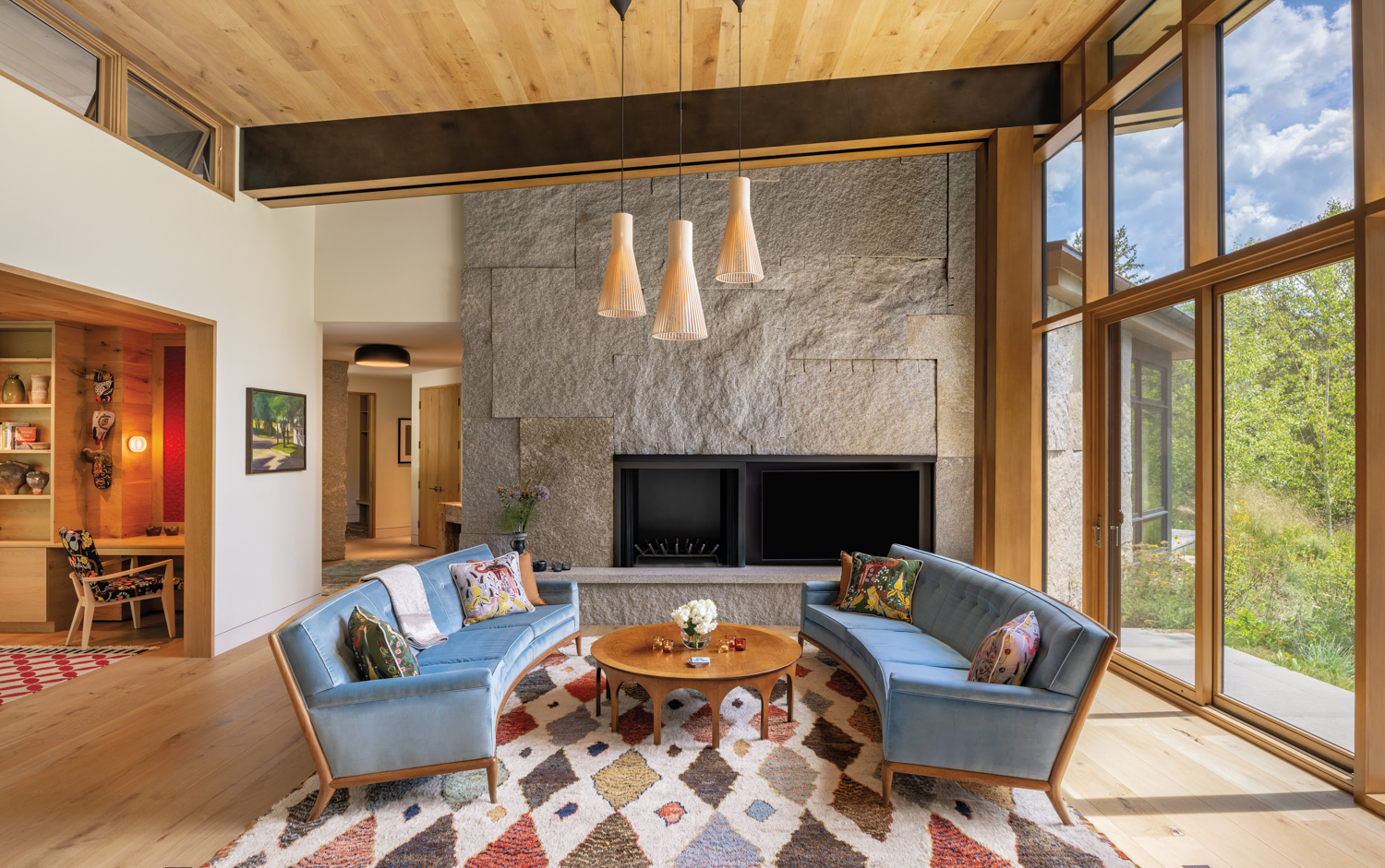 Living room with two light-blue sofas, a geometric rug in soft hues and a large granite fireplace surround