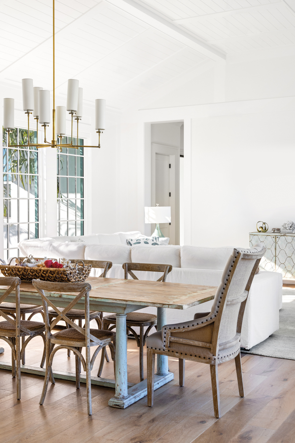 dining area with distressed pine table, wood side chairs, linen head chair, chandelier and white walls