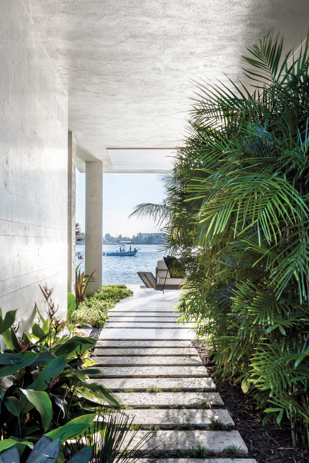 covered limestone breezeway that leads to bayfront loggia with mix of plants