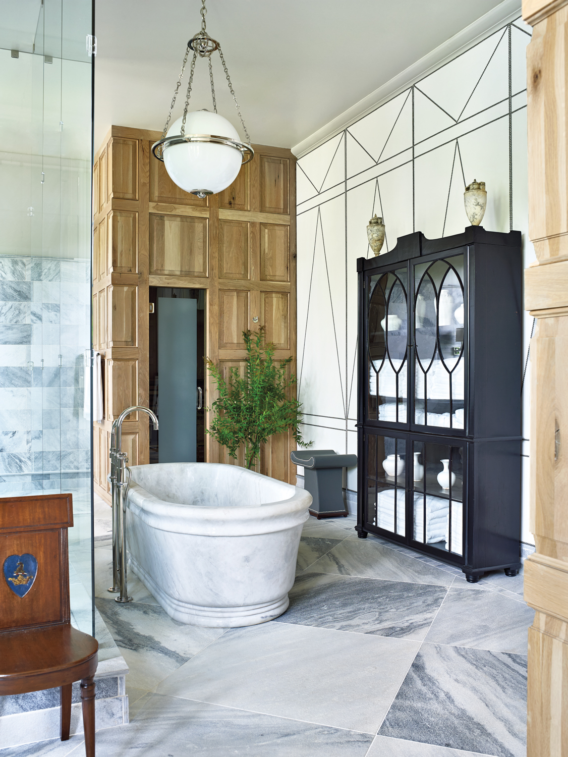 Bathroom with tall black linen cabinet, standalone marble tub and paneled walls