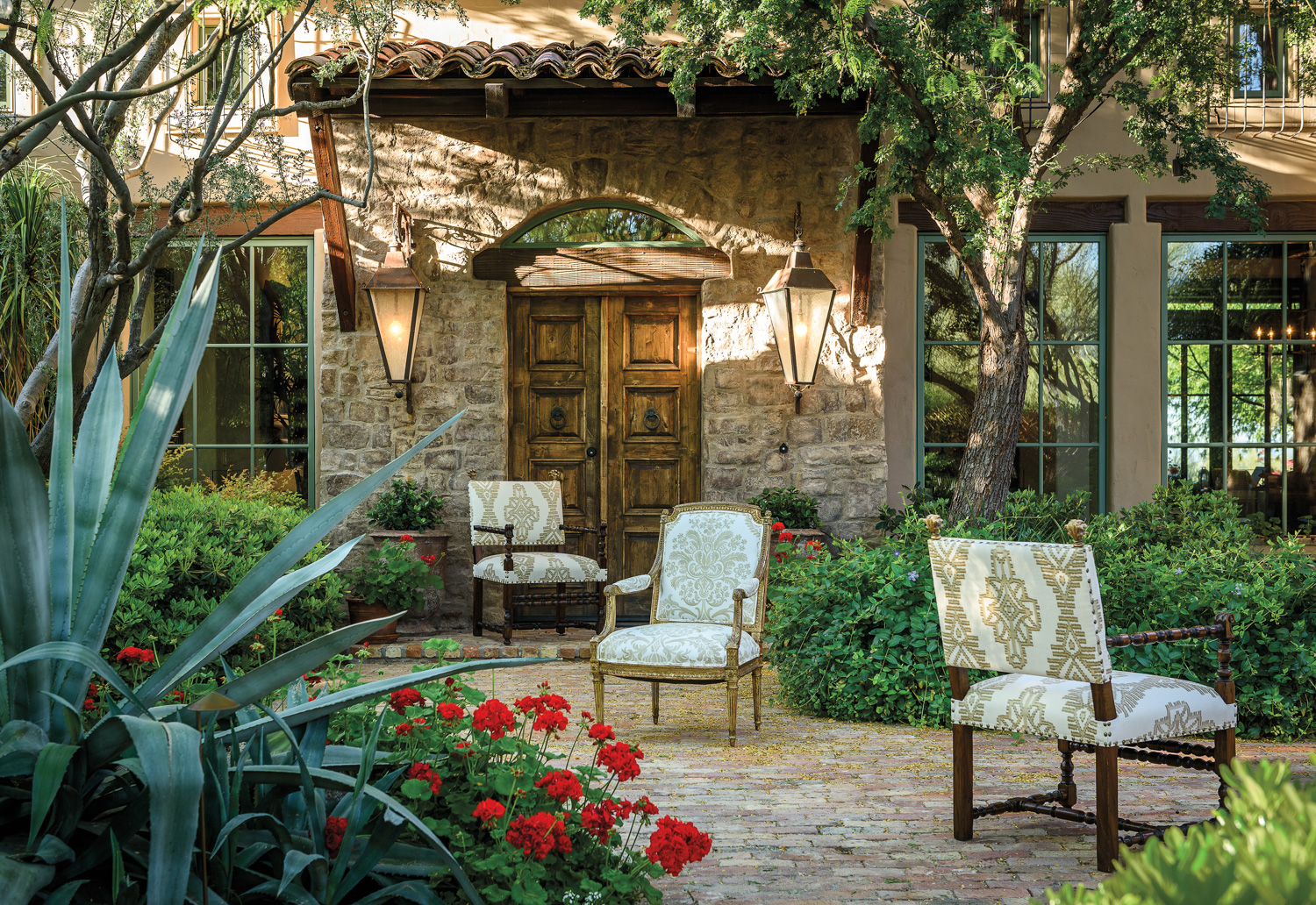 Three upholstered chairs sitting in an outdoor courtyard surrounded by plants.