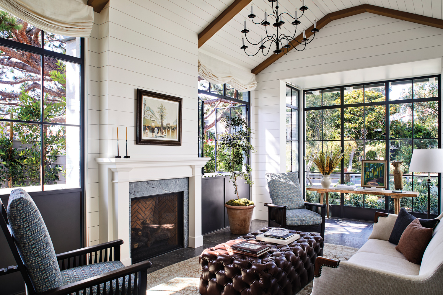 Living room with white paneled walls, steel-framed windows, a fireplace and a leather-tufted ottoman