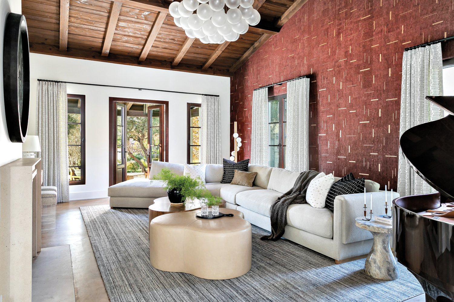Living room with red wall covering with gold details, cloud-shaped chandelier and curvy, neutral-hued furnishings