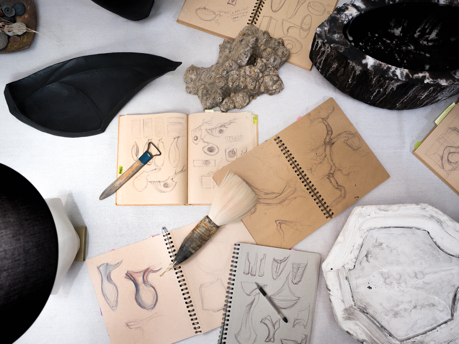 Sketchbooks, brushes, tools and pieces of clay on a table