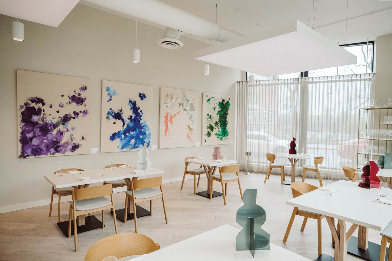 Neutral-colored restaurant with colorful, abstract art on walls.