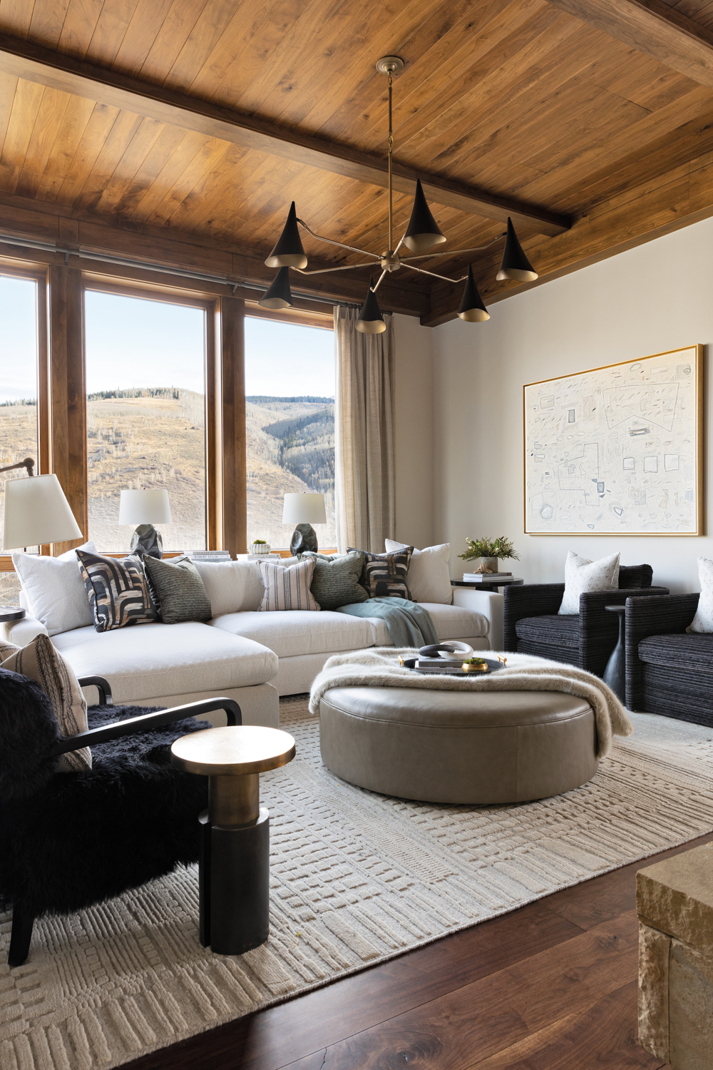 Lounge room with white sectional, round leather ottoman, white rug and mountain views