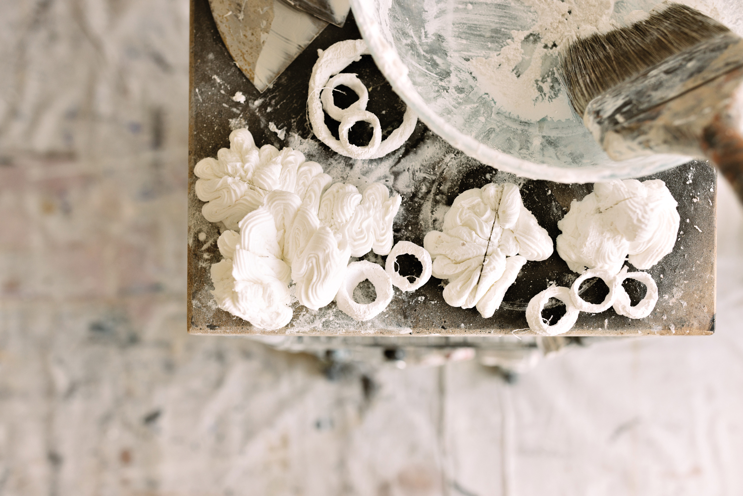 Small sculpted plaster pieces next to a bowl in which plaster is being mixed with a brush