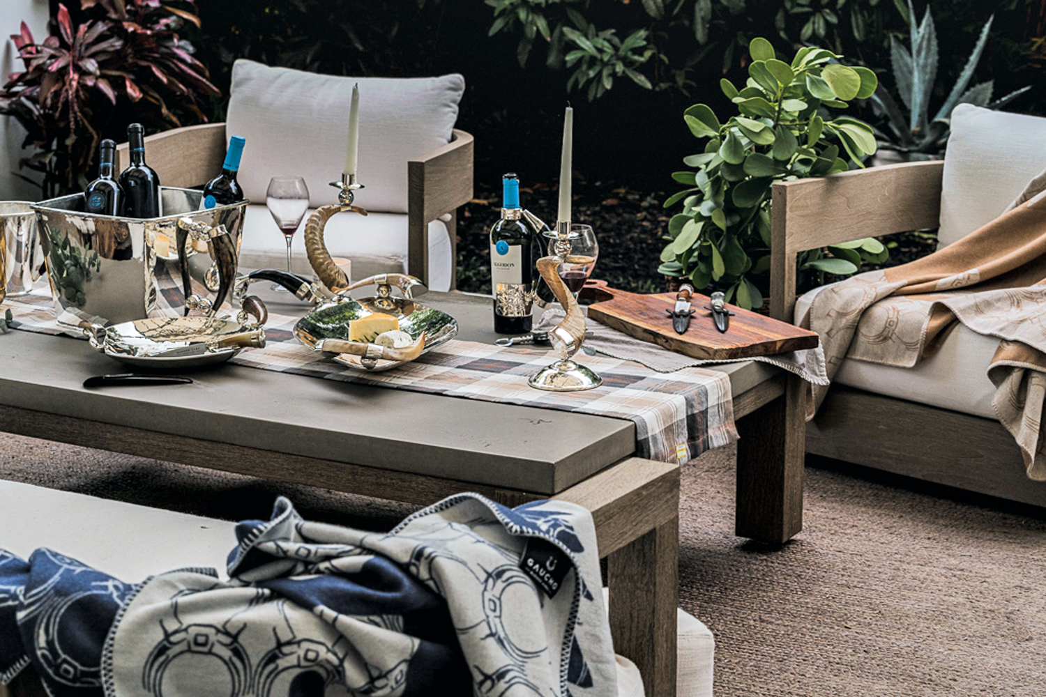 Outdoor patio seating surrounds a table displaying silver-plated trays and sculpted goat horn candle holders