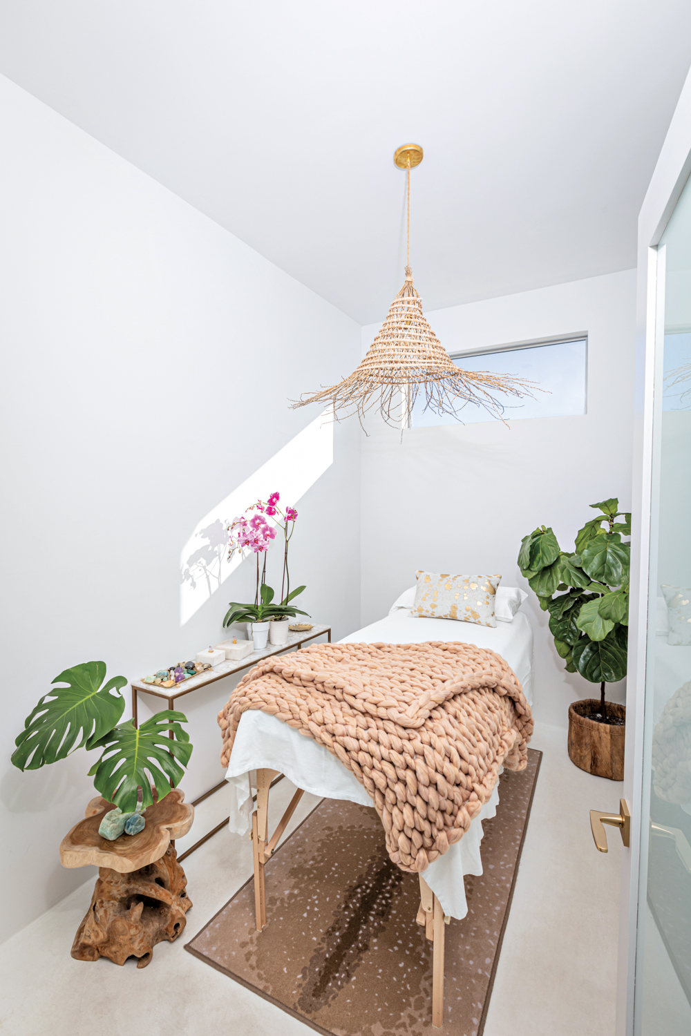 Treatment table with a cream throw blanket in a white room under a rattan-like pendant 