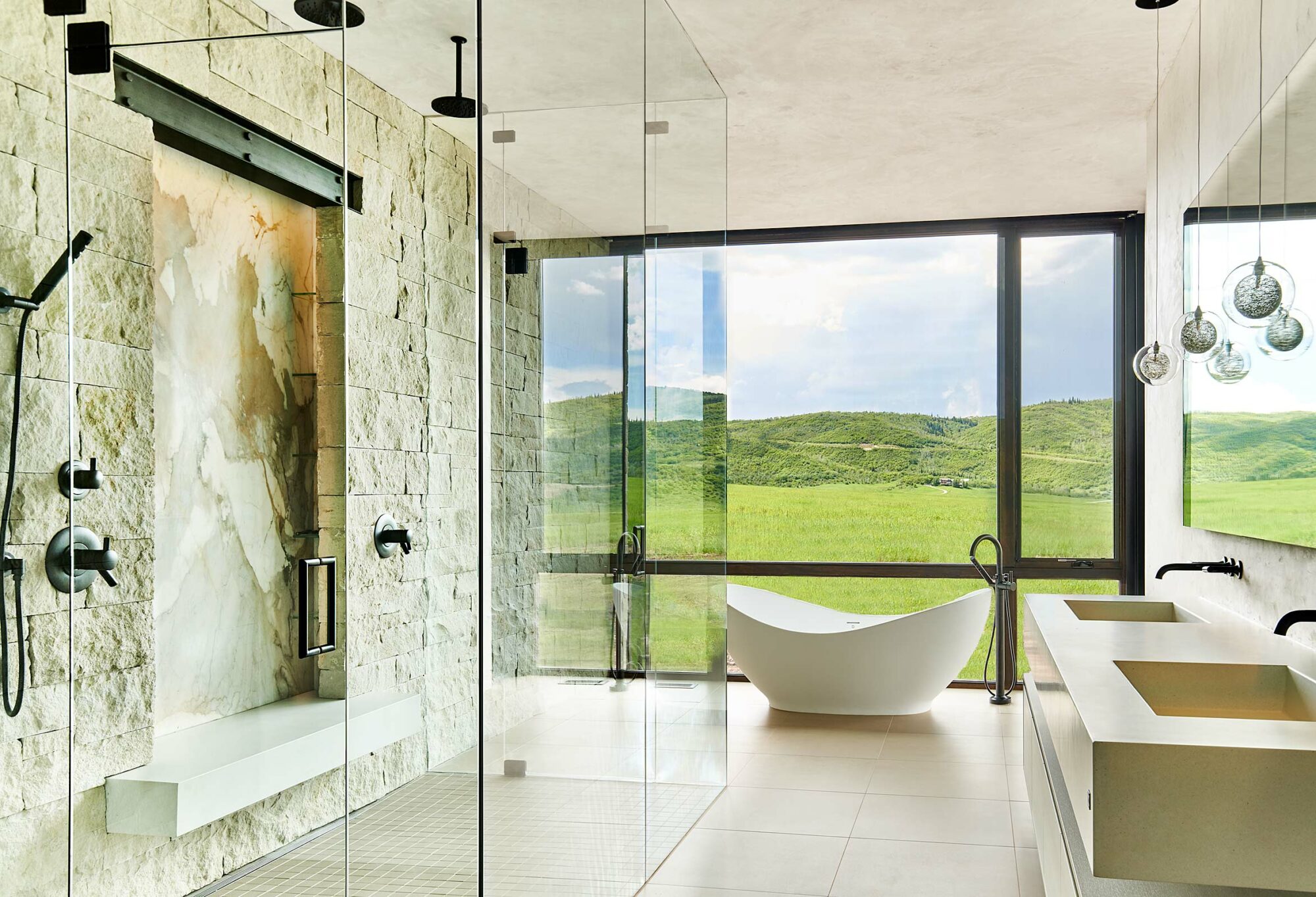 a freestanding tub in front of floor to ceilingTranquil, peaceful bathroom spaces remain a top ask from clients. Soft tones and natural materials help accomplish the look. windows in natural stone bathroom