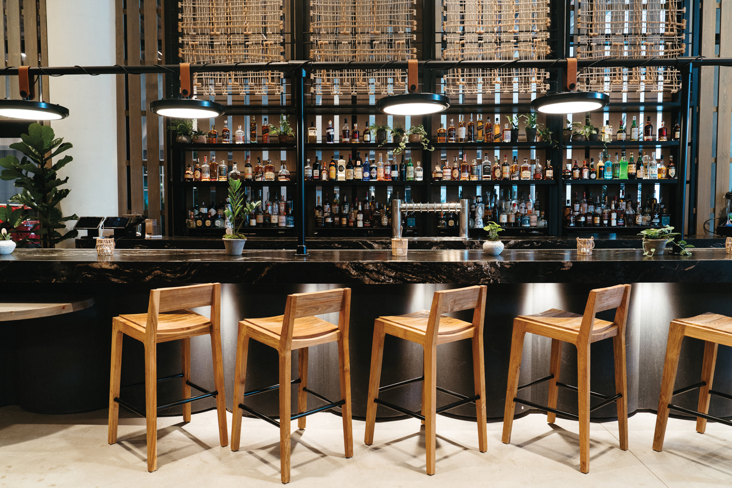 Dark marble hotel bar lined with backed wooden stools