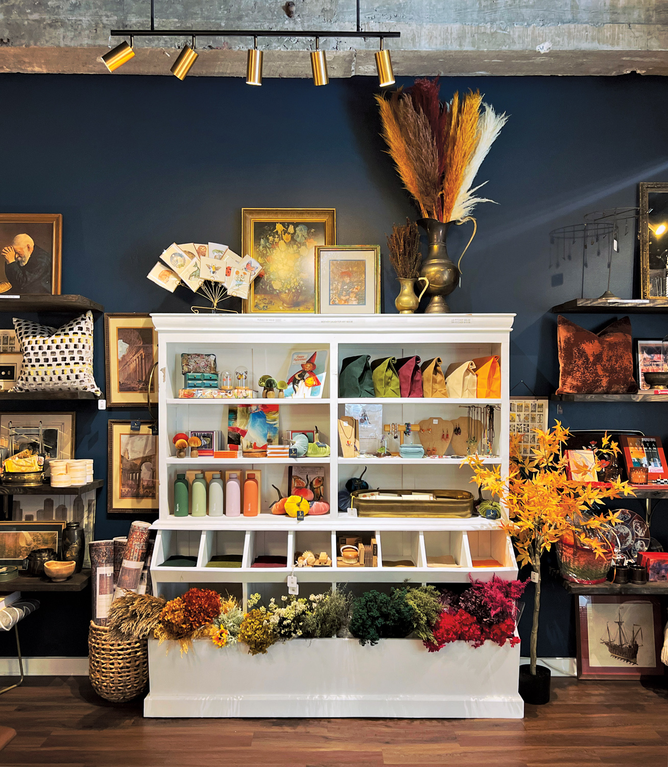 Open white cabinetry against dark blue walls holds colorful dried botanicals and home accessories