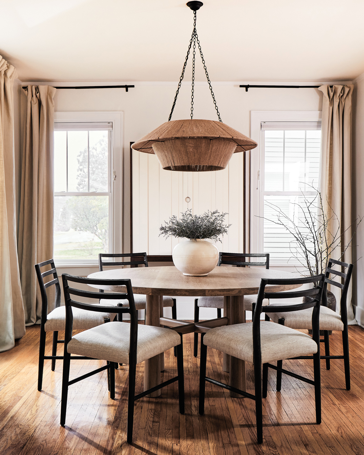 round dining table surrounded by 6 chairs under low-hanging pendant light
