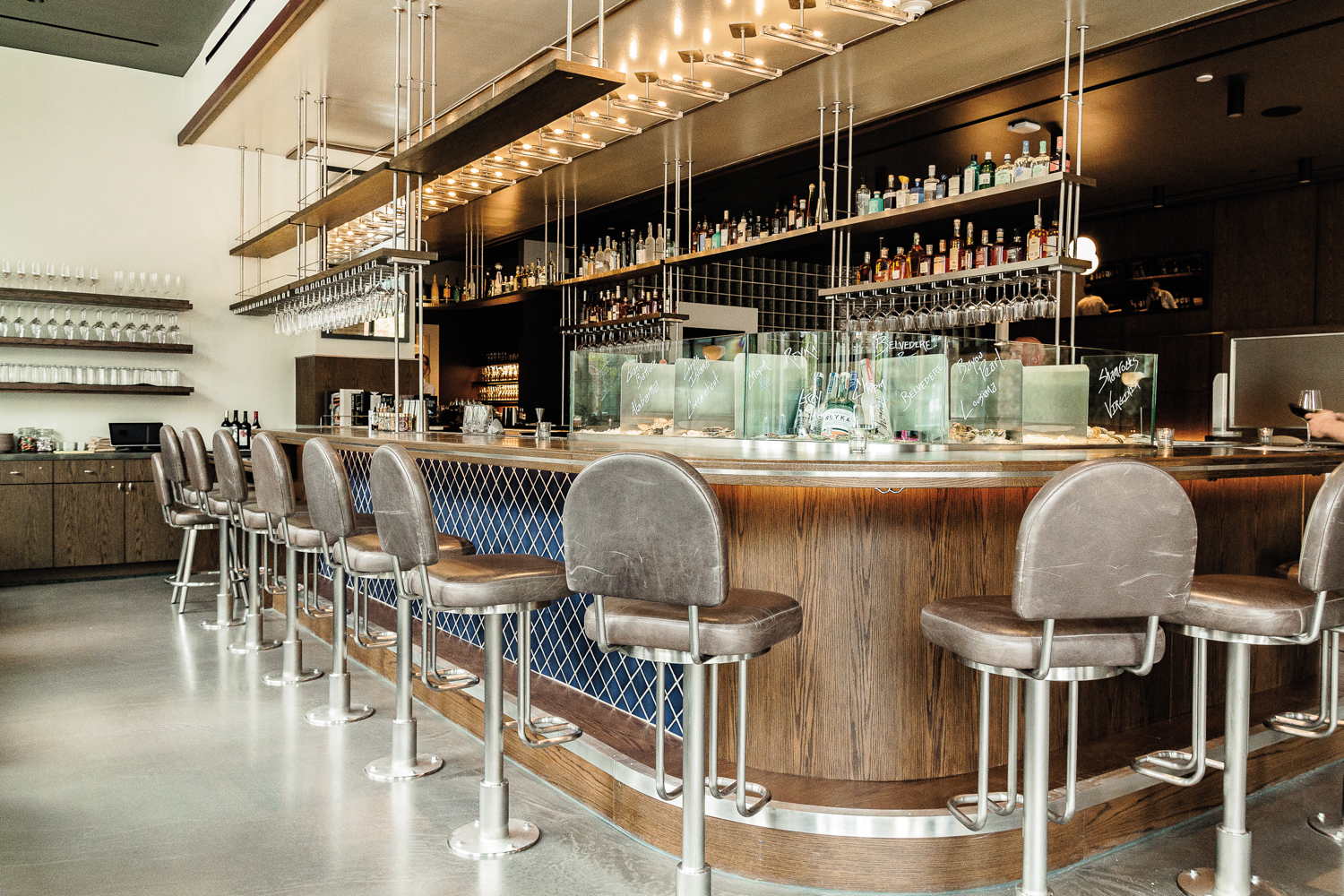 Swivel bar stools line a curved restaurant bar with blue tile in diamond-shaped pattern alongside the front 