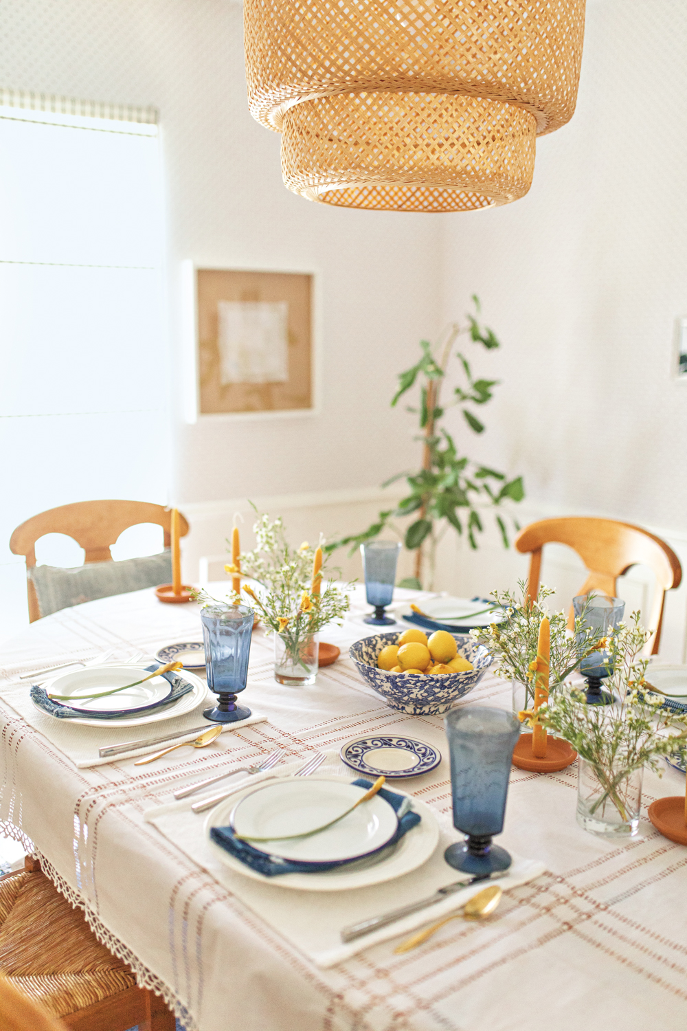 White plates and tall blue glasses are set on a dining room table lined with terra-cotta candle sticks 