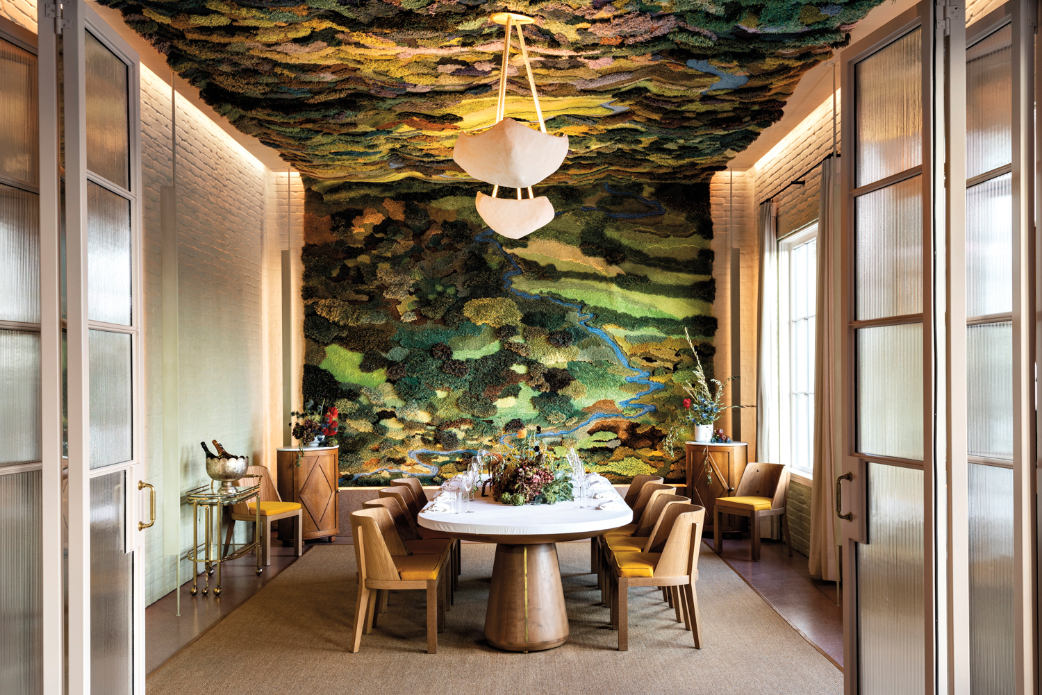 Pendant lights hang from a textile landscape artwork on the ceiling at March restaurant in Houston
