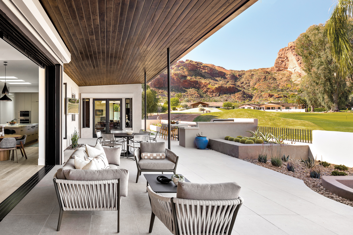 outdoor patio with dining table, sofa and lounge chairs looking out on a golf course and mountains