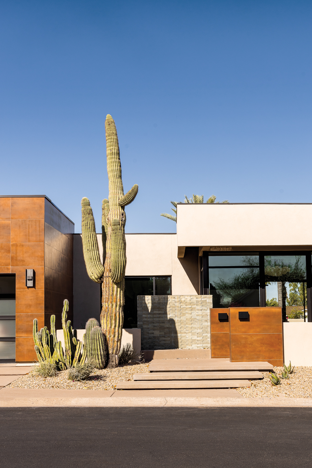 The exterior of a modern home clad in rust-colored porcelain tile and cacti in the yard