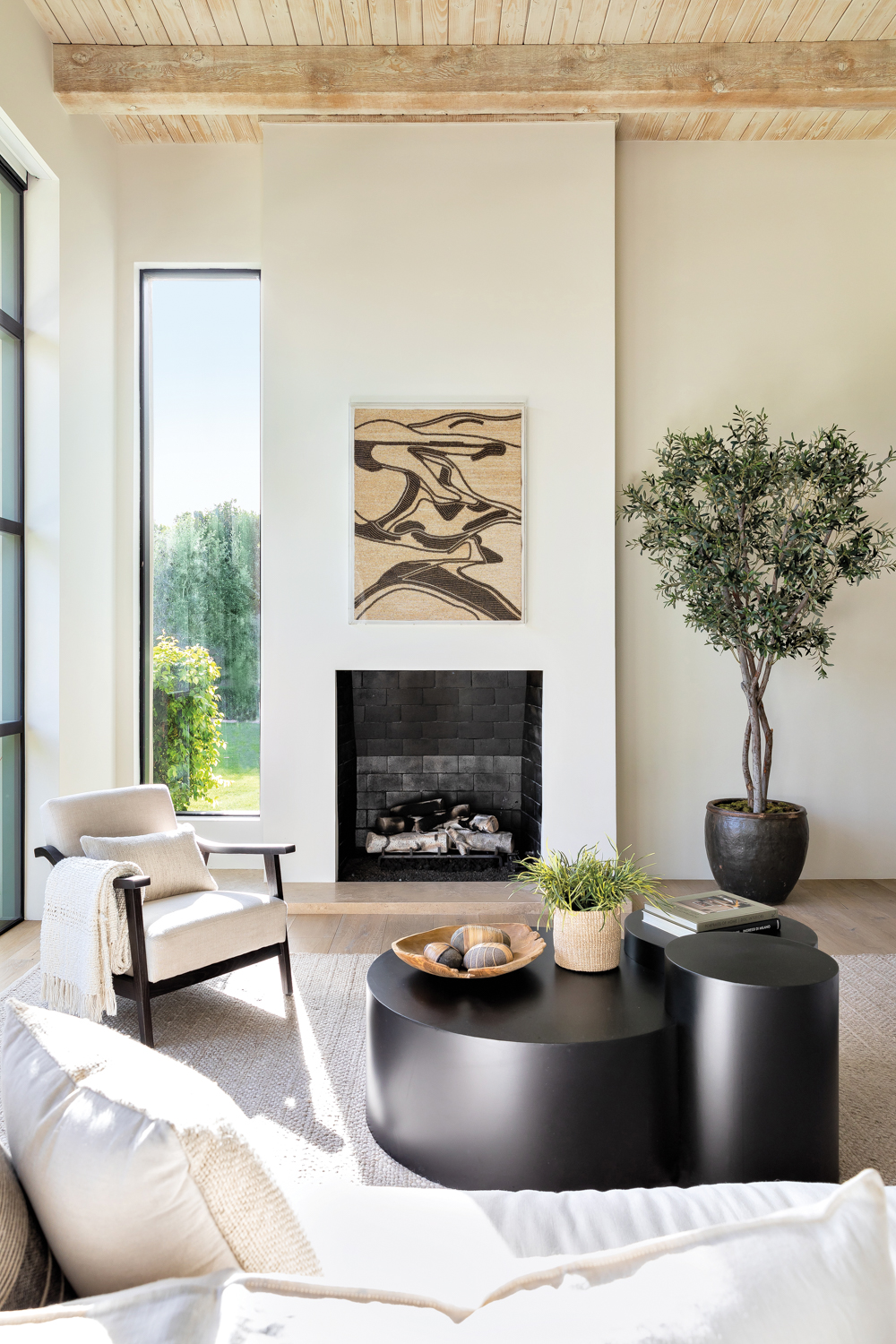 living room with black sculptural coffee table, white armchair and fireplace with abstract artwork above