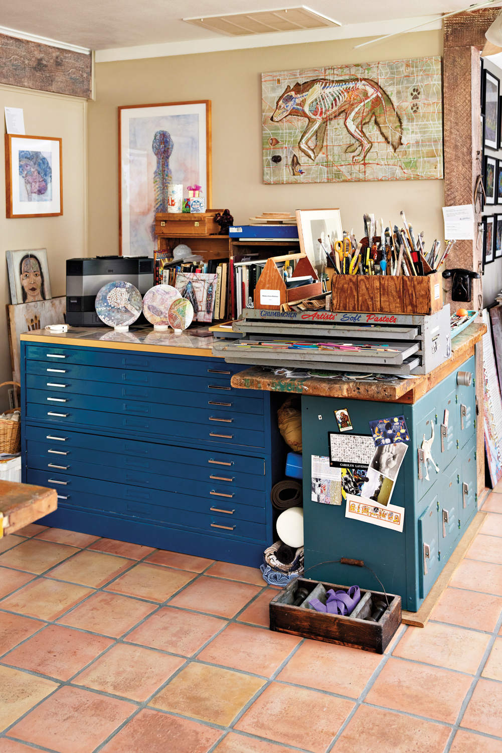 corner of a studio showing flat files, books, artwork, brushes and pencils