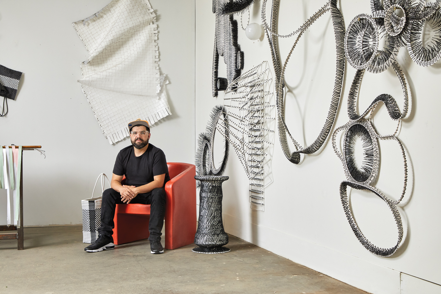 a male in a red chair surrounded by white and black wall sculptures