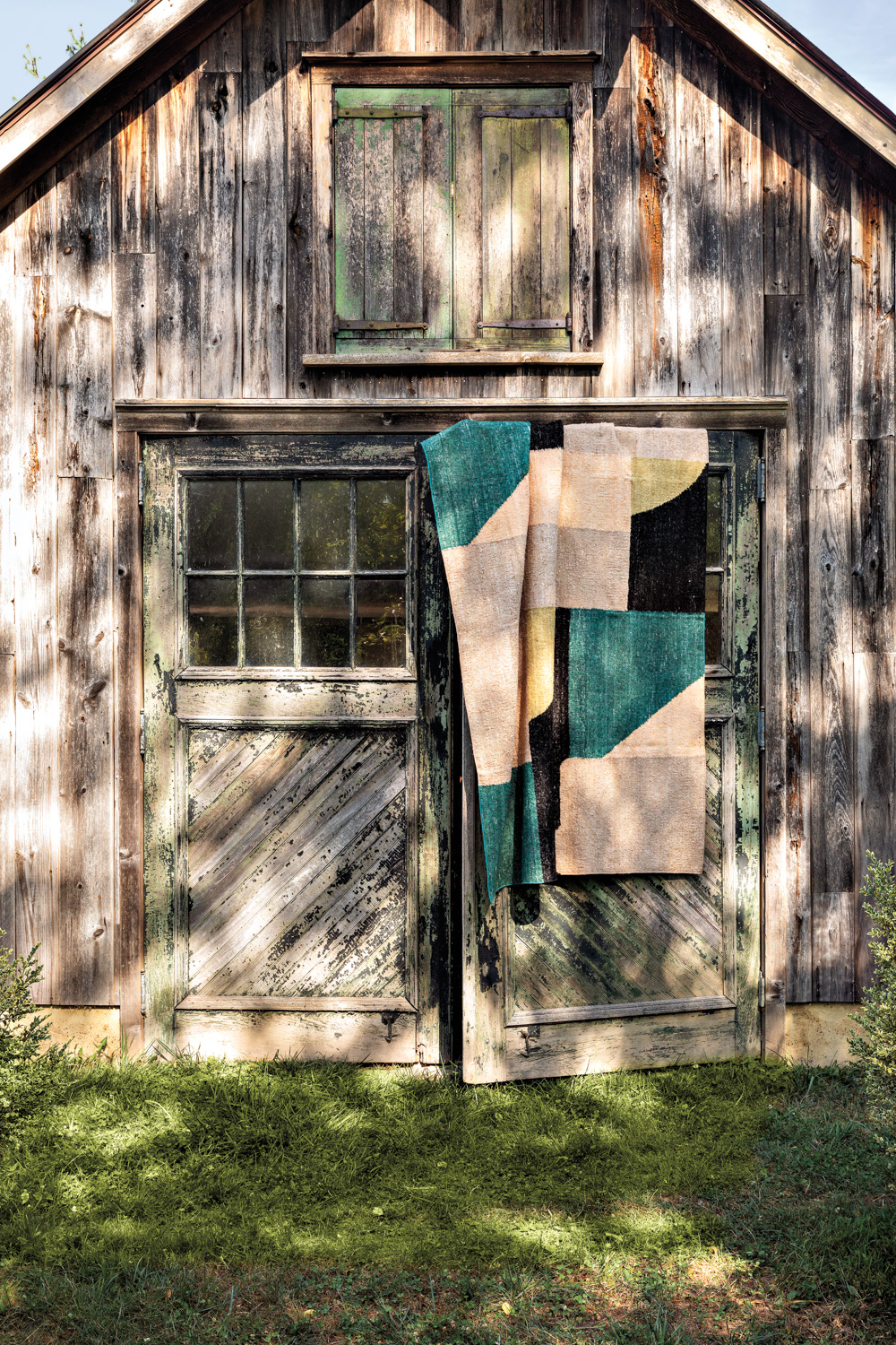 patchwork rug made from silk remnants hangs on a rustic barn window