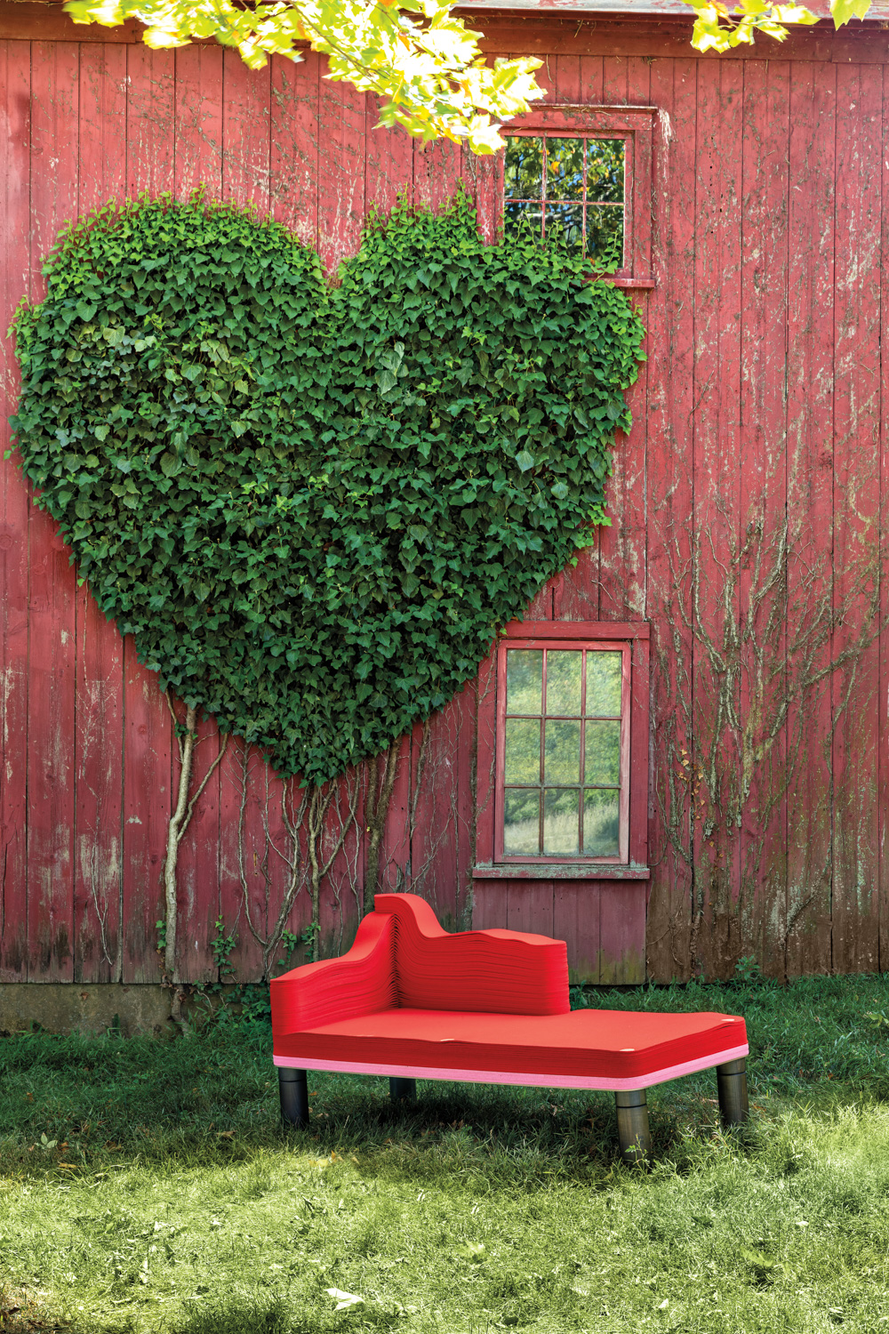 red chaise lounge from repurposed materials in front of red barn with heart landcaping