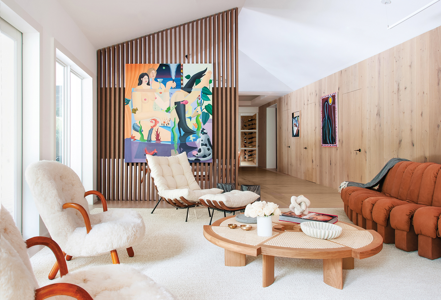 living area with wood screen, vibrant art, white armchairs, lounge chair, white rug and round wood coffee table