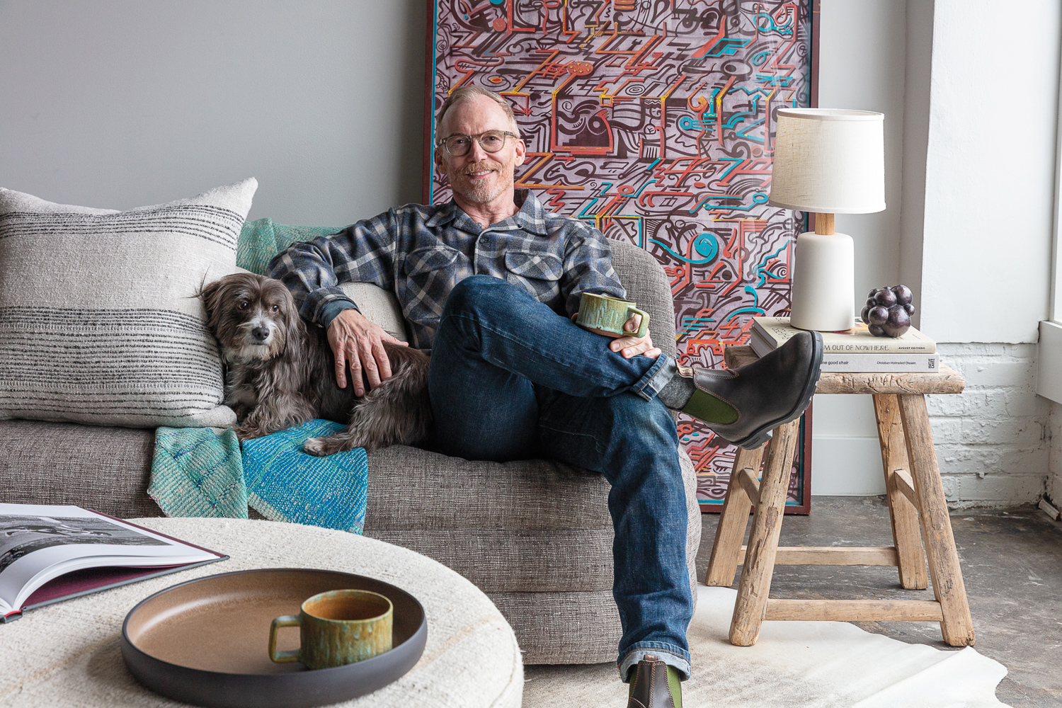 Designer Tim Pfeiffer sitting on a gray sofa with a small gray dog.