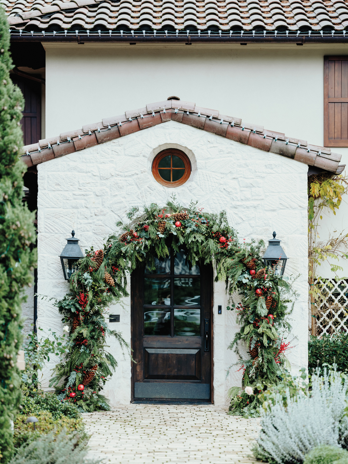 Exterior of white stucco building with archway made of evergreens and red florals over entry