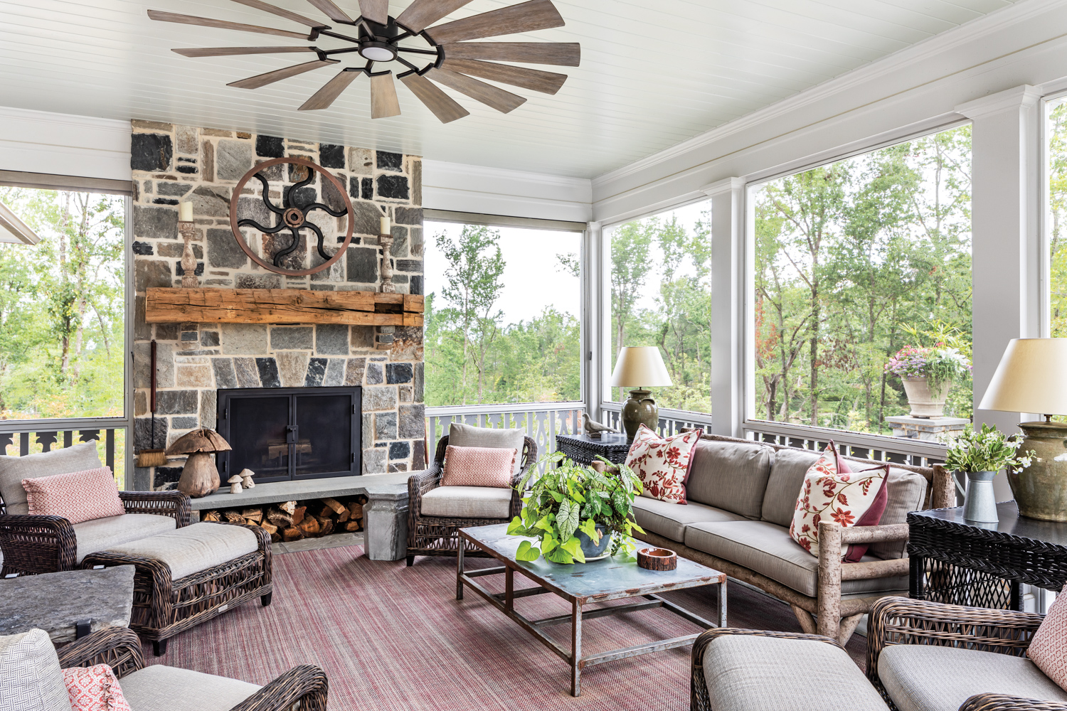Outdoor screened porch with rustic fan, red rug and rugged stone fireplace
