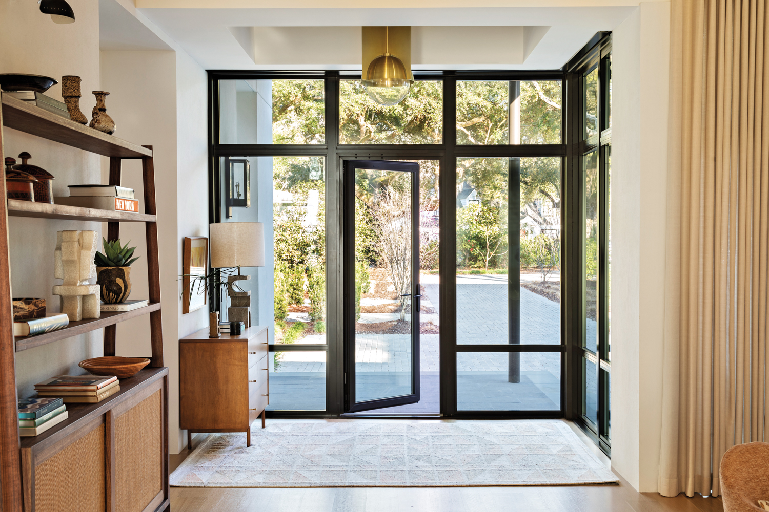 Metal windows and doors allow sunlight to fill a foyer with midcentury-inspired furnishings and lighting