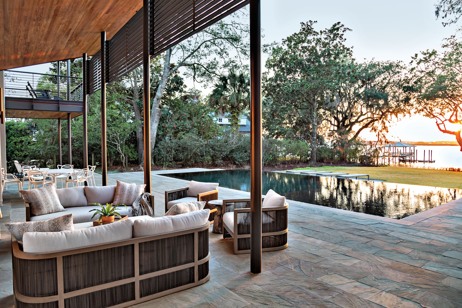 A patio featuring modern furnishings, an infinity pool, live oak trees and river views