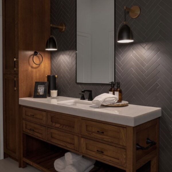 A stylish bathroom with a custom wooden vanity, herringbone tile, and black/gold pendants for mood lighting.